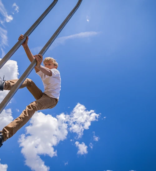Ein Junge auf einem Kletterger&uuml;st im Au&szlig;enbereich der KLIMA ARENA vor blauem Himmel.